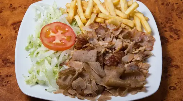 Talerz z prawdziwym kebabem, frytkami, sałatą i pomidorem. Apetyczny posiłek na drewnianym blacie.