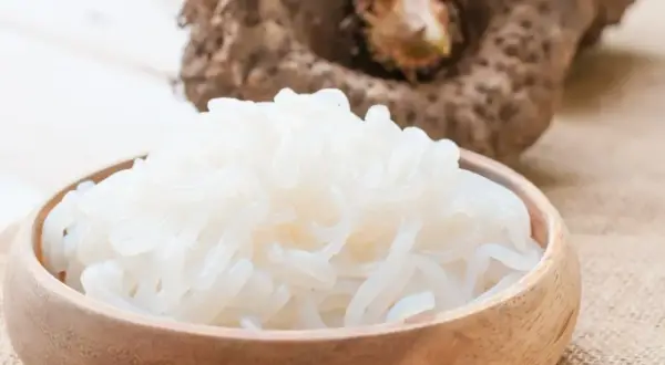 Miseczka pełna białego makaronu z mąki konjac, obok surowa bulwa.