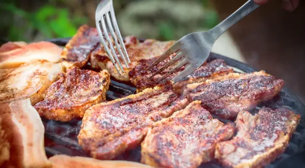 Soczysty boczek na grillu, idealny po marynacie. Dwie widelce sprawdzają stopień wysmażenia.
