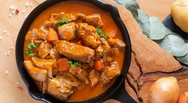 Gulasz z polędwiczki wieprzowej w aromatycznym sosie, z kawałkami marchewki i natki pietruszki, podany w żeliwnej patelni.