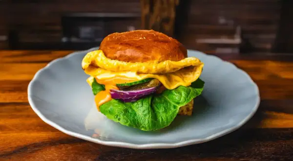 Soczysty burger z serem, sałatą, ogórkiem i czerwoną cebulą na talerzu.