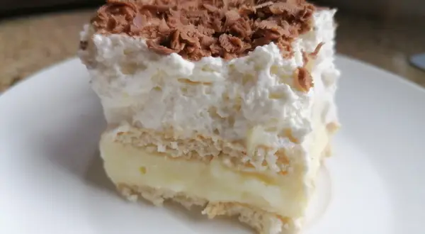 Szybkie ciasto bez pieczenia z budyniem i herbatnikami, przełożone kremem i posypane czekoladą. Idealne na deser!