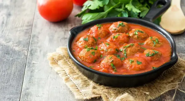 Pyszne pulpeciki w aromatycznym sosie pomidorowym, posypane natką pietruszki. Idealny sos do pulpetów na drewnianym stole.
