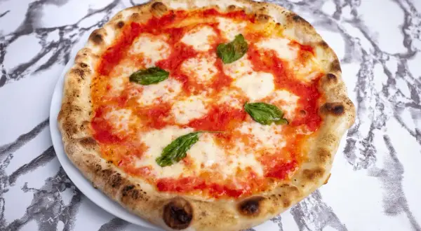 Pyszna pizza napoletana z pomidorami, mozzarellą i bazylią na białym talerzu, na tle marmurowego wzoru.