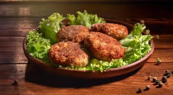 Cztery apetyczne kotlety mielone z airfryer, podane na liściach sałaty, prezentują się wyśmienicie.