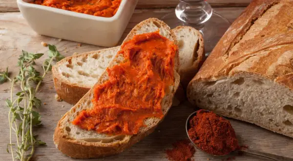 Nduja co to? Pikantna, smarowna kiełbasa na chlebie, obok przyprawy i ziół. Idealna na przekąskę.
