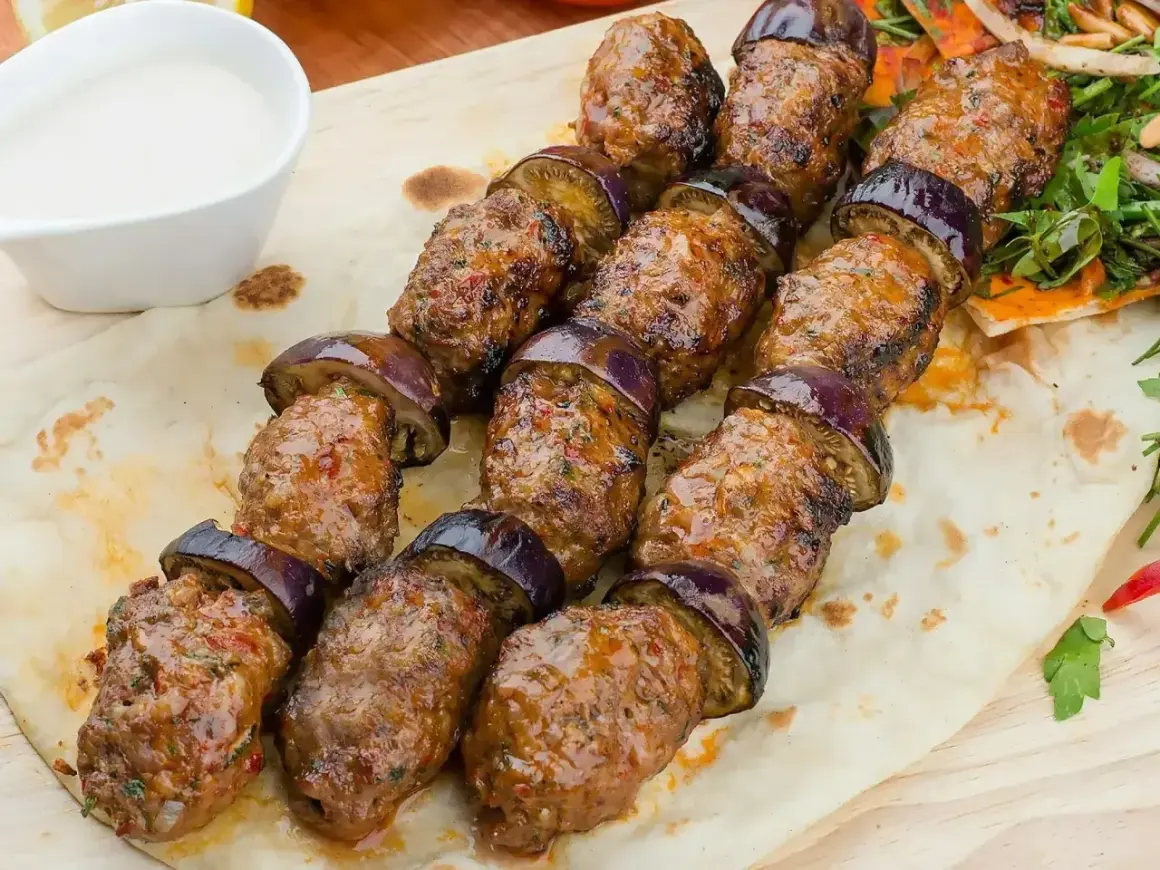 Kofta kebab z bakłażanem na płaskim chlebie, podany z sosem.