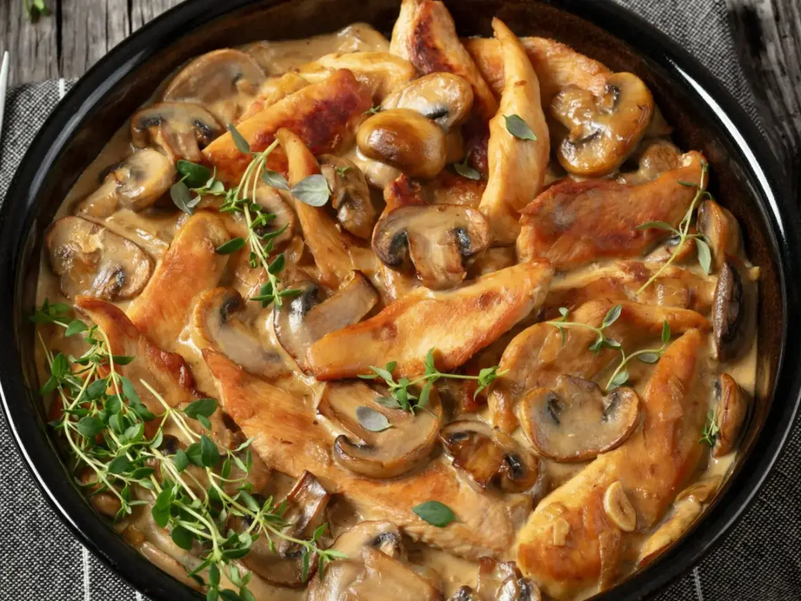 Pyszne polędwiczki z kurczaka w kremowym sosie z pieczarkami, udekorowane świeżym tymiankiem.