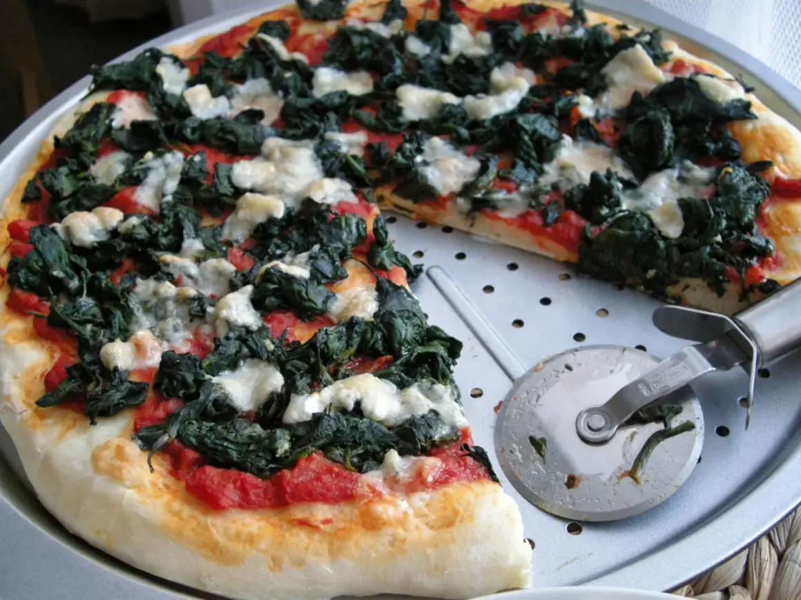 Pyszna pizza ze szpinakiem i białym serem, gotowa do pokrojenia.
