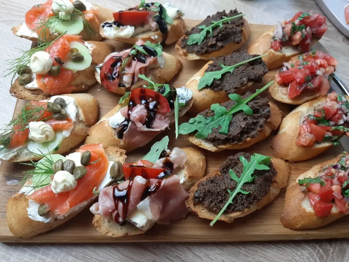Tanie przekąski na imprezę: bruschetty z łososiem, szynką parmeńską, pastą z oliwek i pomidorami. Idealne na każdą okazję!
