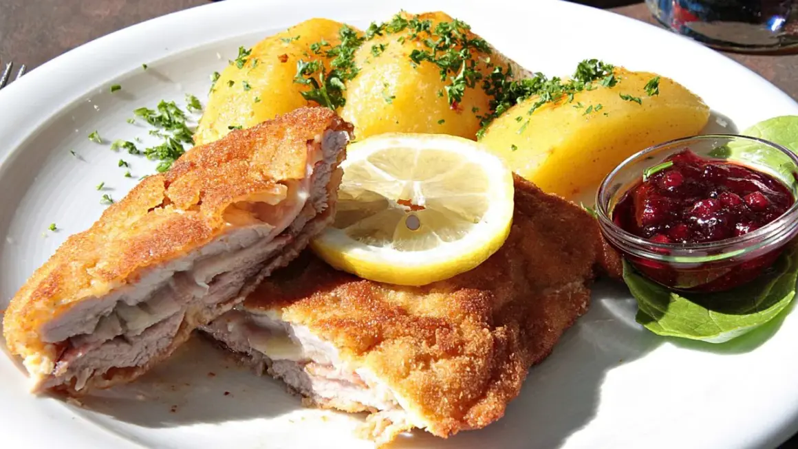 Pyszny kotlet po szwajcarsku, podany z ziemniakami, plasterkiem cytryny i żurawiną.