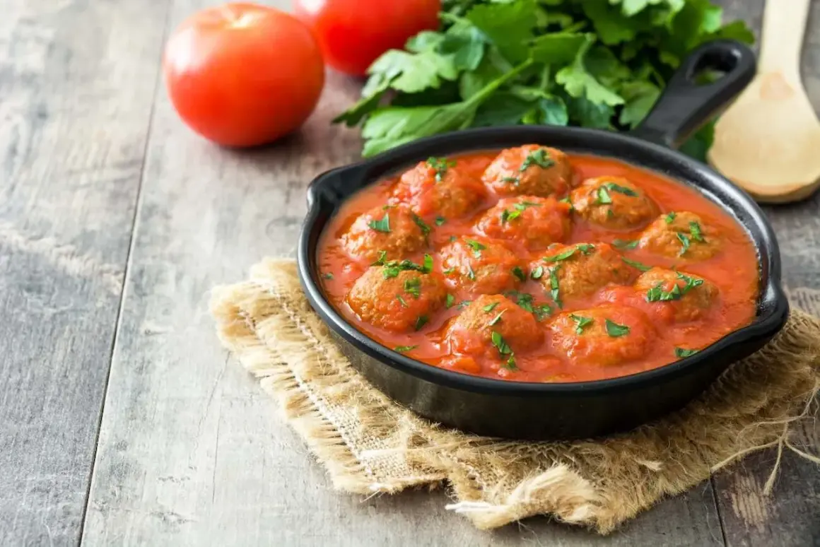 Pyszne pulpeciki w aromatycznym sosie pomidorowym, posypane natką pietruszki. Idealny sos do pulpetów na drewnianym stole.