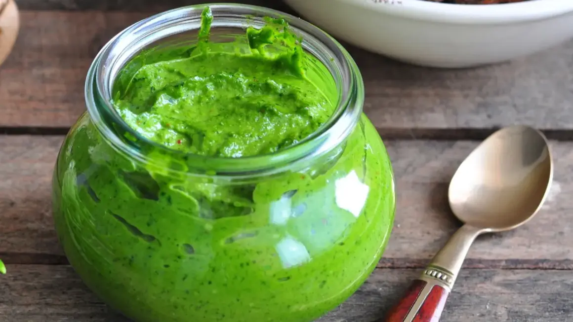 Słoik pełen intensywnie zielonego pesto z pietruszki, gotowego do użycia. Obok leży złota łyżeczka.
