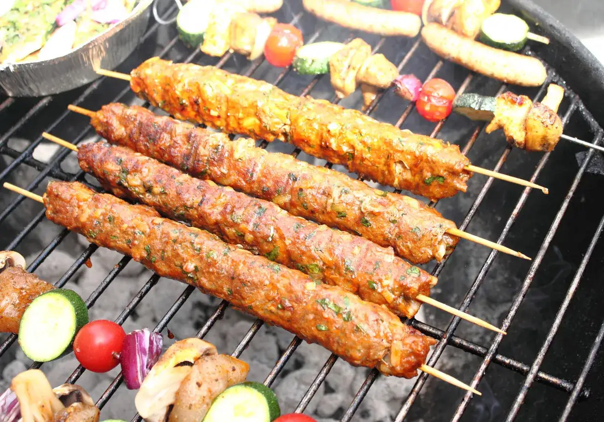 Cztery soczyste kofta kebab na patyczkach grillują się z warzywami.