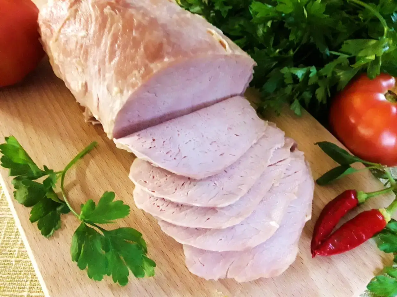 Schab gotowany w majonezie, pokrojony w plastry, z pomidorami, papryczkami chili i natką pietruszki na desce.