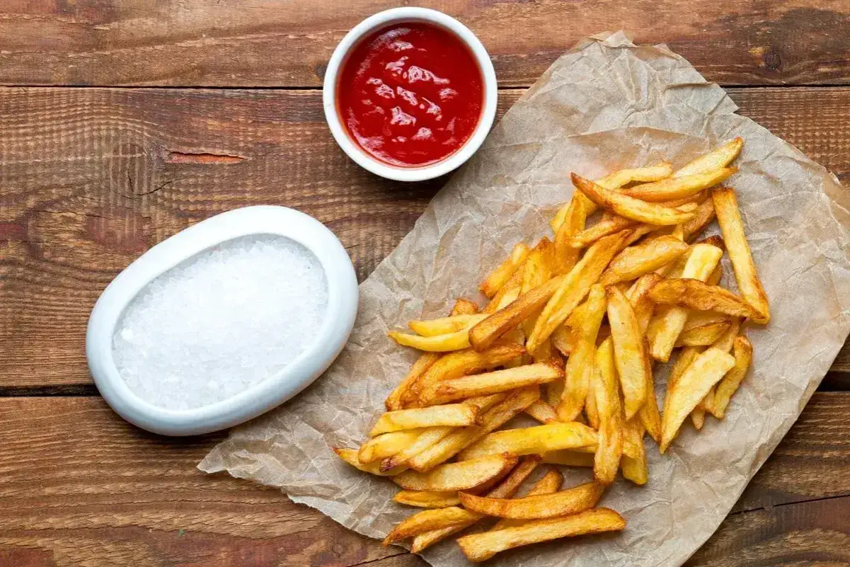 Złociste frytki mcdonald kcal na papierze, obok miseczka ketchupu i sól. Idealne na szybką przekąskę.