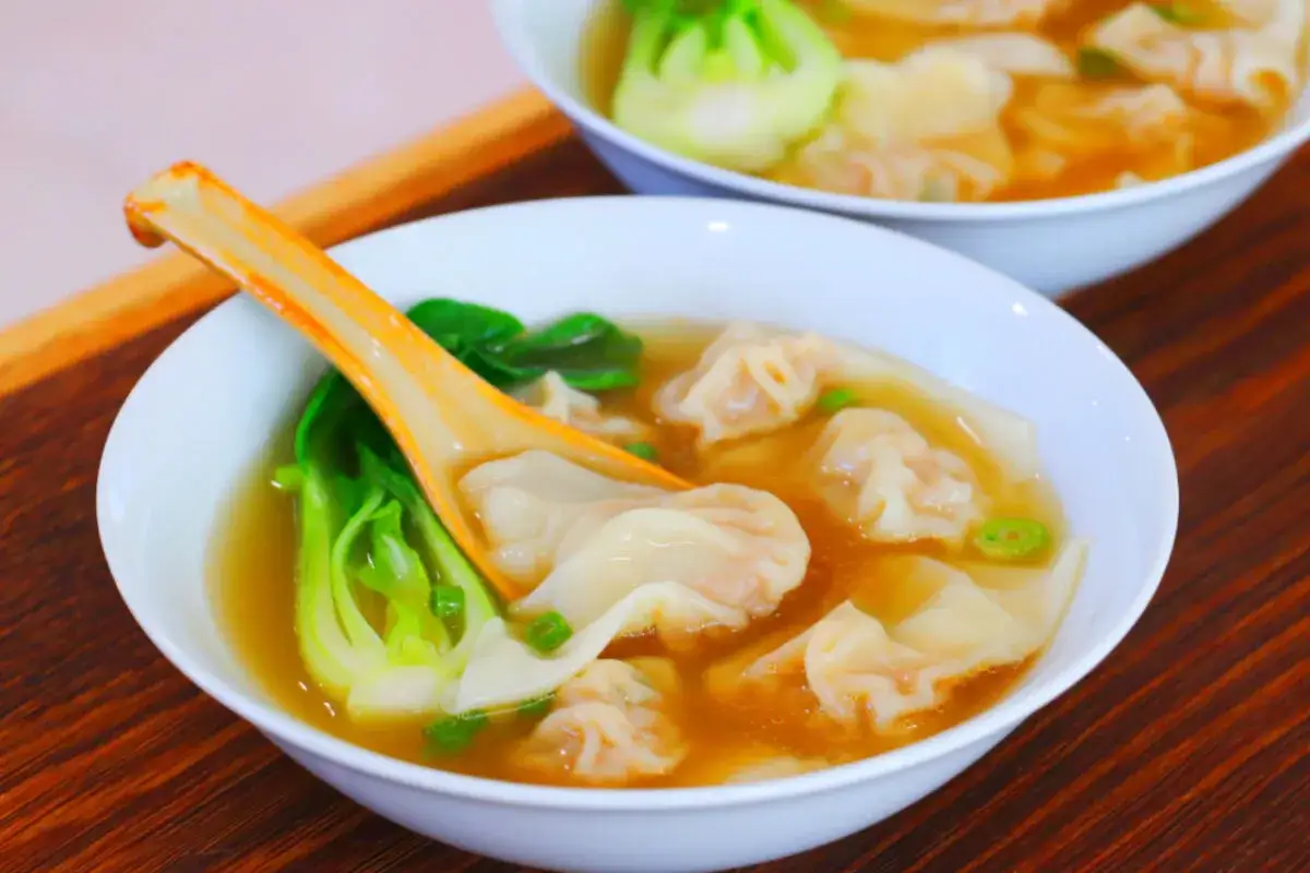 Aksamitna zupa wonton z zielonymi warzywami i pomarańczową łyżką.