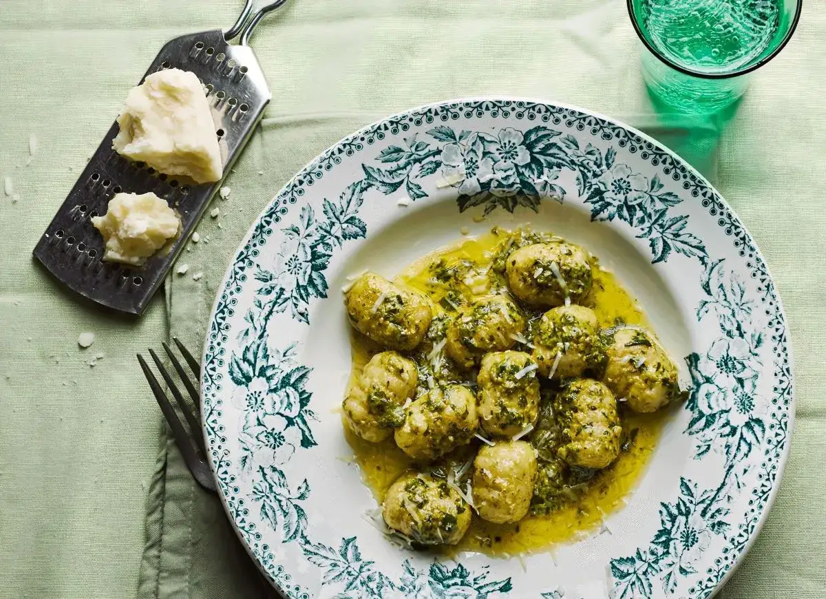 Pyszne gnocchi z pesto, polane oliwą i posypane parmezanem, czekają na talerzu. Obok tarka z kawałkiem sera.
