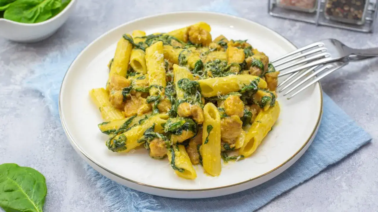 Penne z kurczakiem i szpinakiem w kremowym sosie, posypane parmezanem. Pyszne danie gotowe do spożycia.