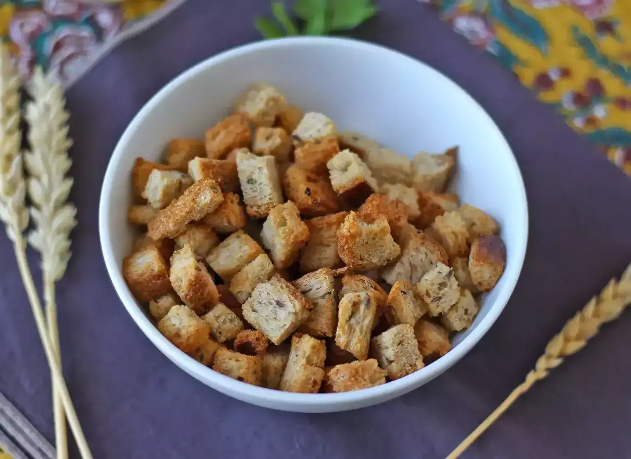 Chrupiące grzanki z airfryer w miseczce, obok kłosy zboża. Idealne do zup i sałatek.