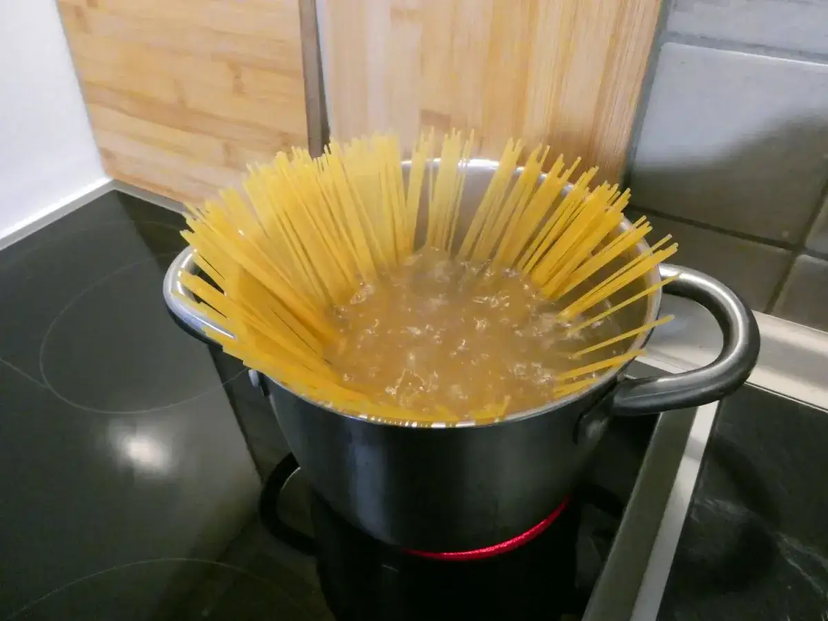 Długi makaron spaghetti gotuje się w garnku z wrzącą wodą. To pierwszy krok, jak ugotować makaron.