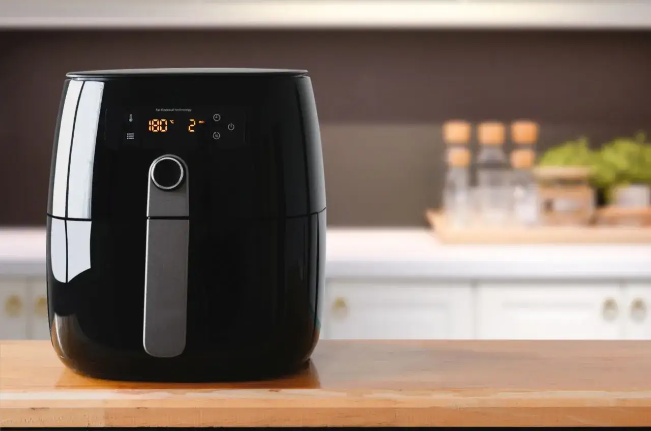 Czarna frytkownica beztłuszczowa na drewnianym blacie, idealna do zdrowego gotowania. Sprawdź nasz ranking air fryer!