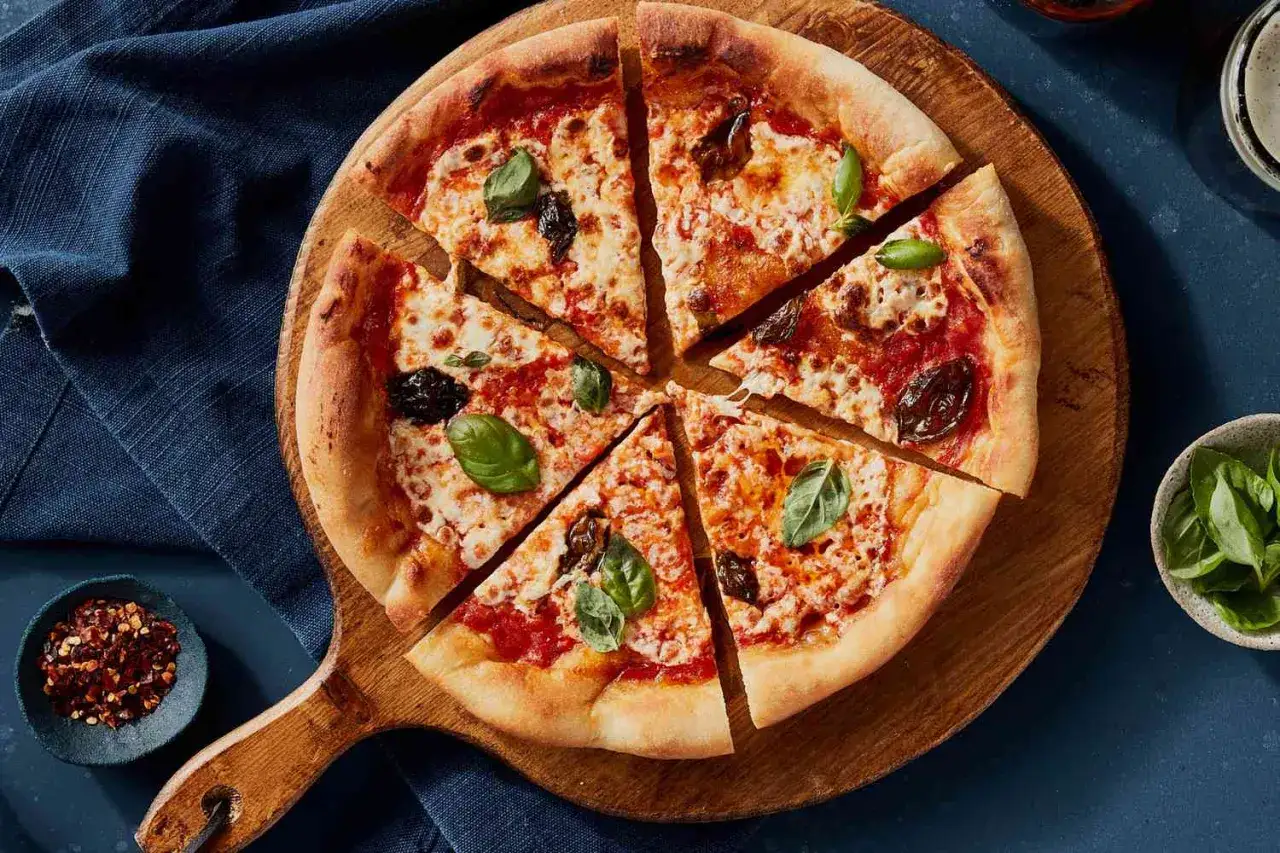 Pyszna pizza margerita z bazylią i pomidorami, pokrojona na kawałki, na drewnianej desce.