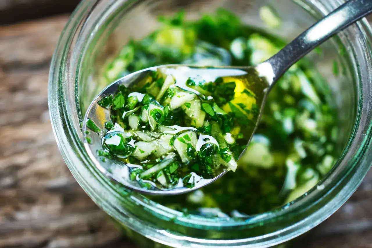 Łyżka pełna aromatycznego pesto z pietruszki, zanurzona w słoiku pełnym zielonej, świeżej pasty.