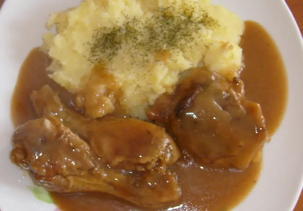Pyszny kurczak w sosie z ziemniakami puree, posypany koperkiem. Danie wygląda apetycznie i sycąco.