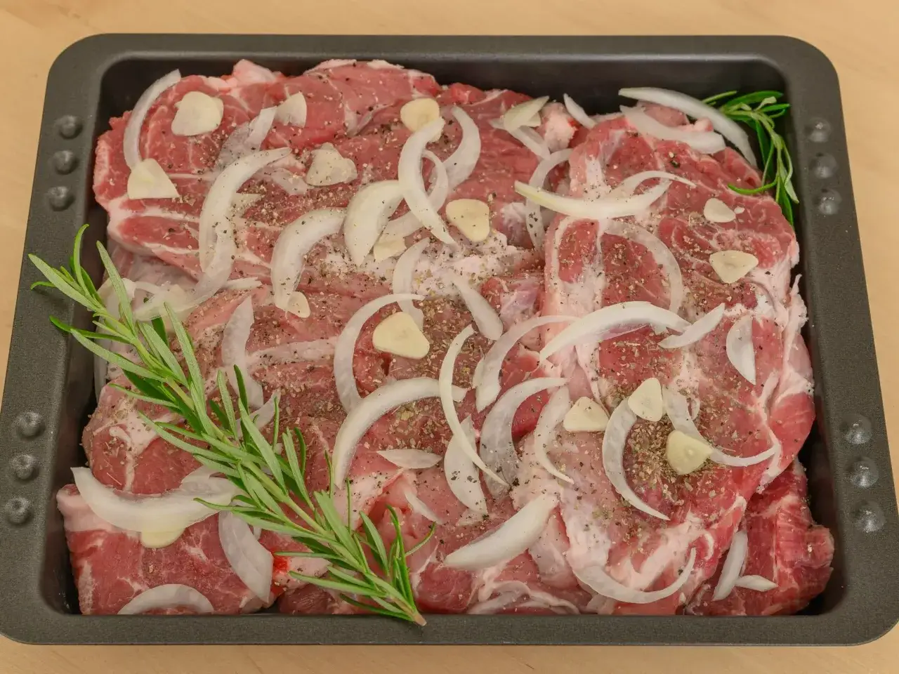 Plastry karkówki z piekarnika, doprawione cebulą, czosnkiem i rozmarynem, gotowe do pieczenia.