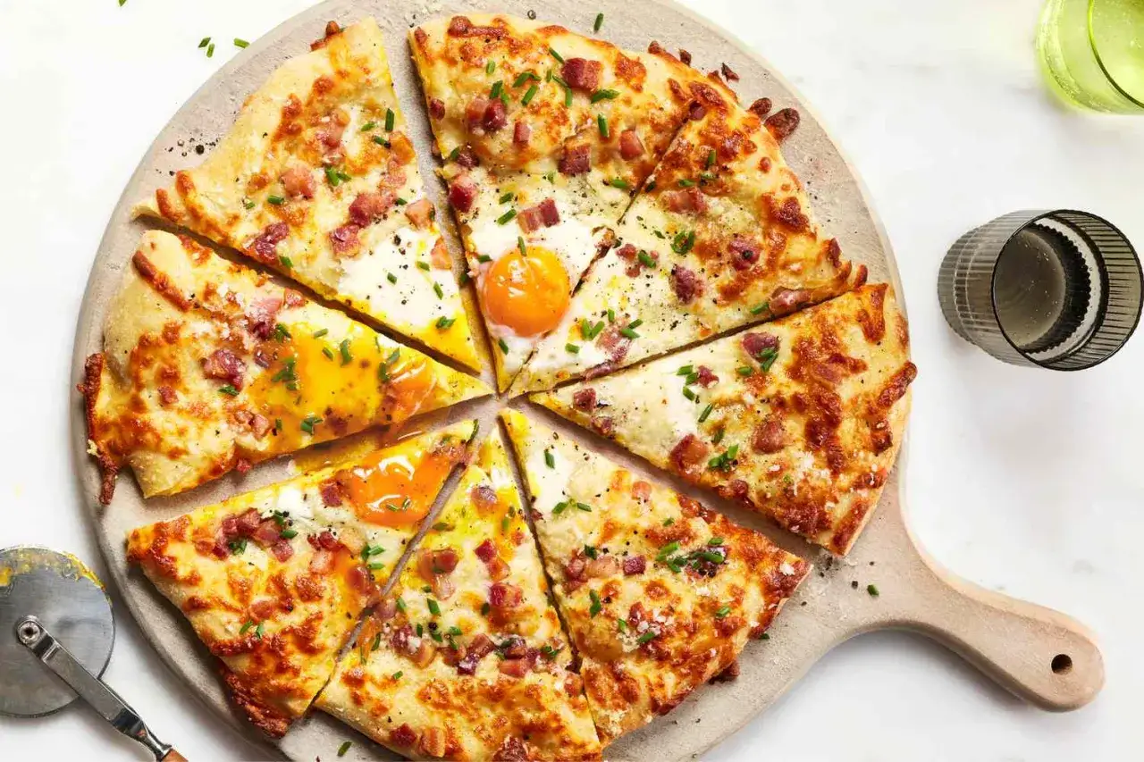 Pizza carbonara z jajkiem sadzonym, boczkiem i szczypiorkiem, pokrojona na kawałki, prezentuje się apetycznie.