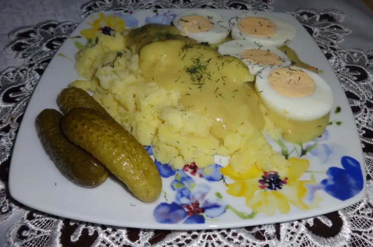 Jajka w sosie musztardowym z ziemniakami i ogórkami kiszonymi na talerzu z kwiatowym wzorem.