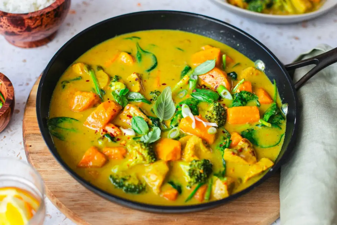 Aksamitne curry z dynią i brokułami, doprawione aromatyczną przyprawą curry, podane w czarnej patelni.