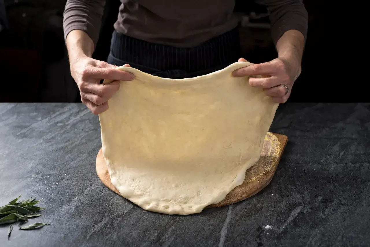 Ręce rozciągają elastyczne ciasto na pizzę. To idealny, szybki przepis na ciasto do pizzy, które zachwyci każdego.