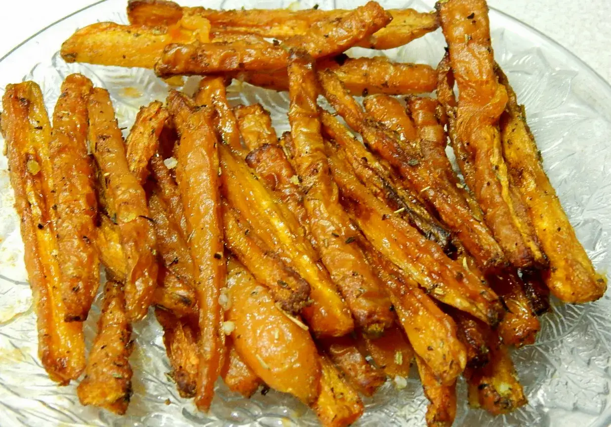 Chrupiące, pieczone frytki z marchewki, doprawione ziołami i przyprawami, podane na szklanej tacy.