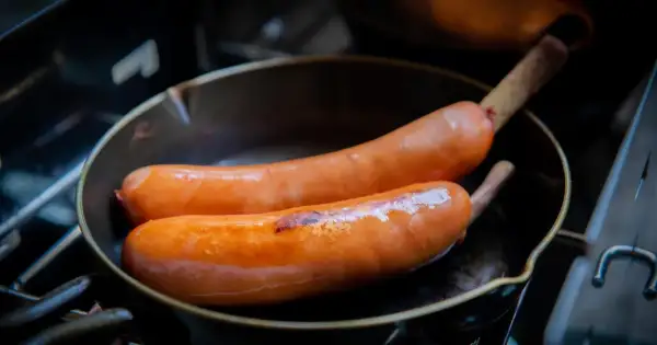 Dwie soczyste kiełbaski smażą się na patelni. Idealne do podania z cebulą, tworzą pyszne danie.
