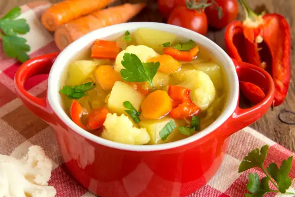 Aromatyczna zupa jarzynowa kcal, pełna warzyw: marchewki, ziemniaków, kalafiora i papryki, ozdobiona natką pietruszki.