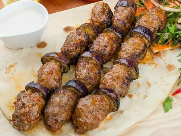 Kofta kebab z bakłażanem na płaskim chlebie, podany z sosem.