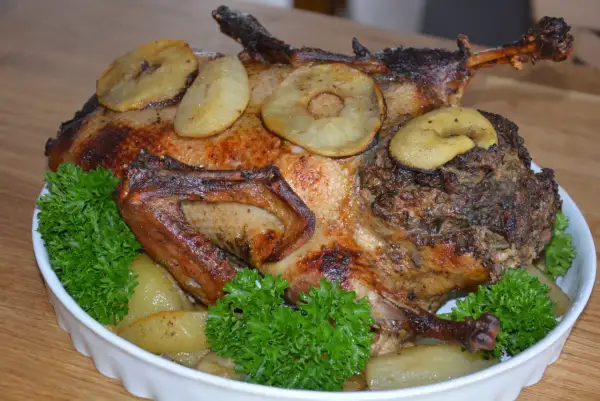 Pieczona kaczka z jabłkami i tradycyjnym nadzieniem do kaczki, udekorowana natką pietruszki.