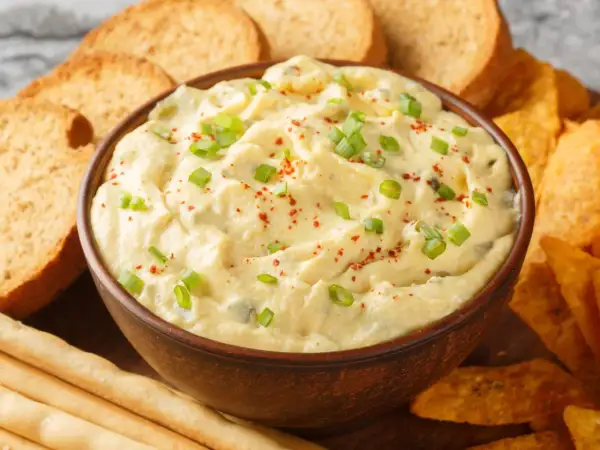 Kremowy dip z zieloną cebulką i papryką, otoczony chrupiącymi grzankami, nachos i paluszkami. Idealny do zanurzania!