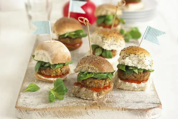 Mini burgery z kotletem, sałatą i flagietkami na desce.
