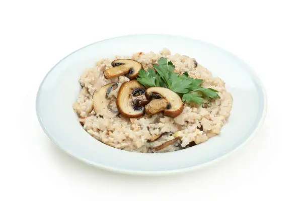 Kremowy ryż do risotto z pieczarkami i natką pietruszki na jasnoniebieskim talerzu.