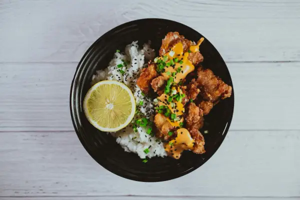 Chrupiące karaage z ryżem, polane sosem i posypane szczypiorkiem, z plasterkiem cytryny.