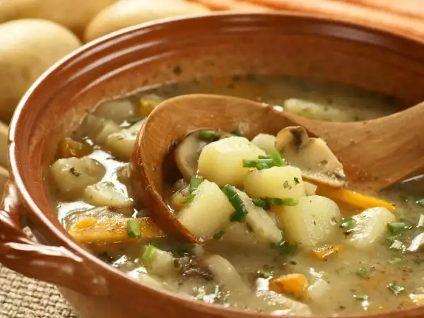 Zupa ziemniaczana przepis babci. Aromatyczna, domowa zupa z ziemniaków, marchewki i grzybów, podana w glinianej misce z drewnianą łyżką.