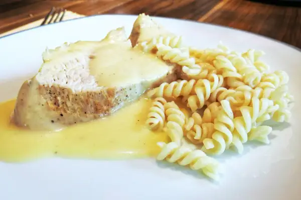 Kawałek pieczonego mięsa w kremowym sosie do potrawki, podany z makaronem fusilli.