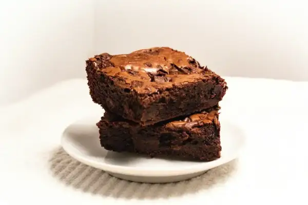 Dwa wilgotne kawałki ciasta brownie z płynną czekoladą, ułożone na białym talerzyku.