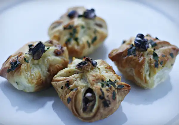 Cztery apetyczne paczuszki z ciasta francuskiego z gruszką i serem pleśniowym, posypane ziołami.