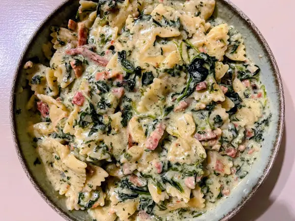 Pyszny makaron farfalle w kremowym sosie ze szpinakiem mrożonym i kawałkami boczku.