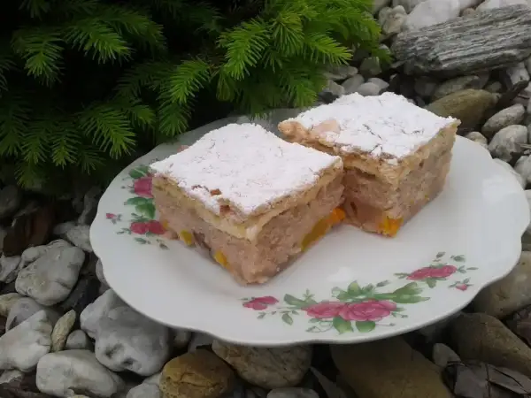 Dwa kawałki ciasta z kisielem na oleju, posypane cukrem pudrem, na talerzyku z różami, wśród kamieni i gałązek choinki.