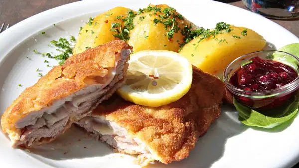 Pyszny kotlet po szwajcarsku, podany z ziemniakami, plasterkiem cytryny i żurawiną.